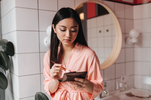 Молодая женщина в розовом халате делает макияж