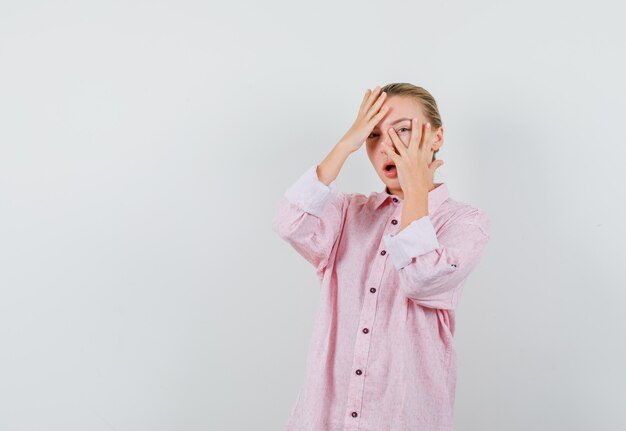 Young woman in pink shirt looking through fingers