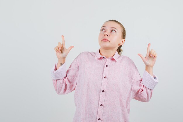 Young woman in pink shirt pointing up and looking focused