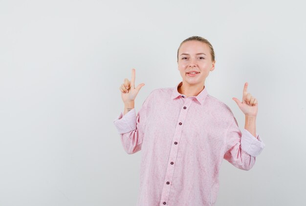 Young woman in pink shirt pointing up and looking glad