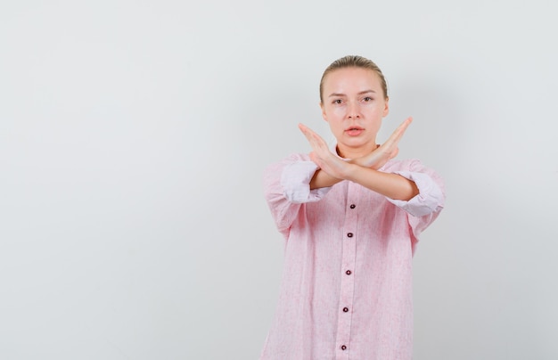 Young woman in pink shirt showing stop gesture and looking exhausted