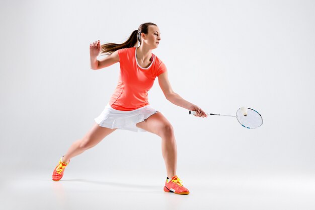 Young woman playing badminton over white wall