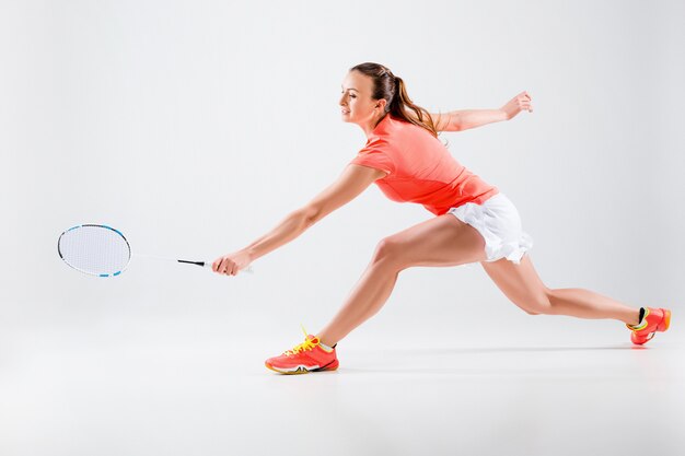 Young woman playing badminton over white wall