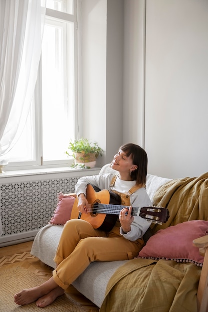 Giovane donna che suona la chitarra in casa con spazio di copia