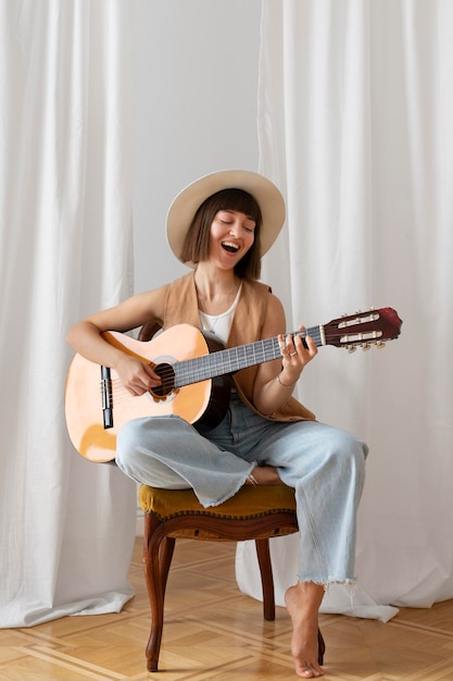 Foto gratuita giovane donna che suona la chitarra al chiuso