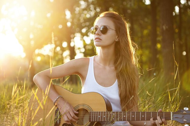 日没時に自然の中でギターを弾く若い女性