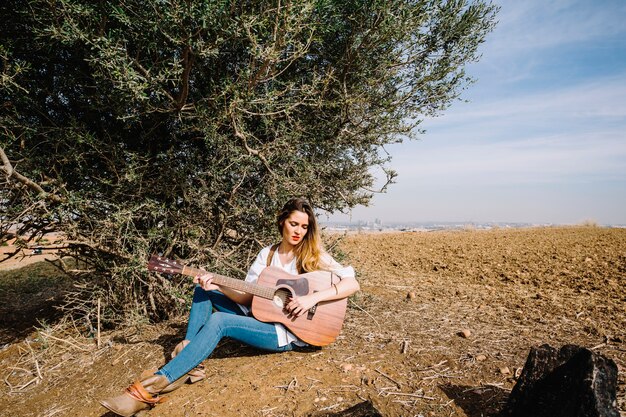 Young woman playing guitar near bush