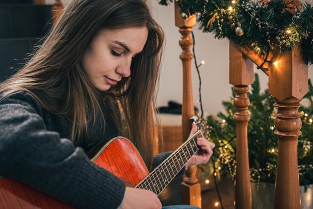 A young woman playing guitar sitting on the steps at home