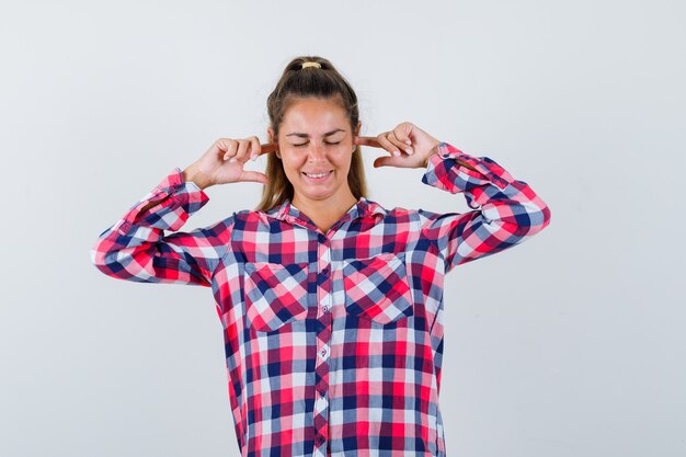 Молодая женщина затыкает уши пальцами в повседневной рубашке и выглядит весело. передний план.