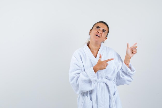 Young woman pointing aside in bathrobe and looking happy