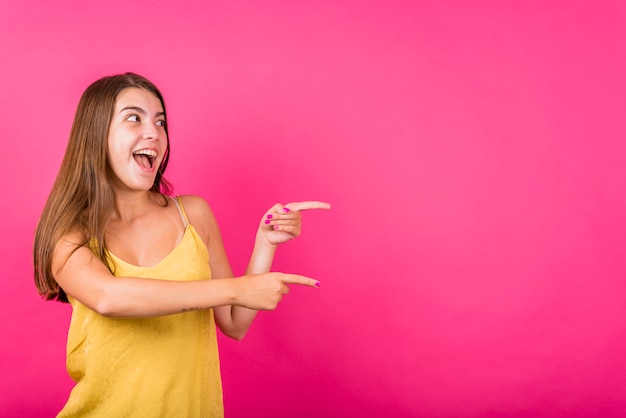 Free photo young woman pointing away on pink background