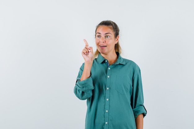 Young woman pointing back in blue shirt and looking curious