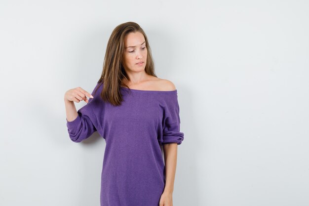 Young woman pointing down in violet shirt and looking focused. front view.