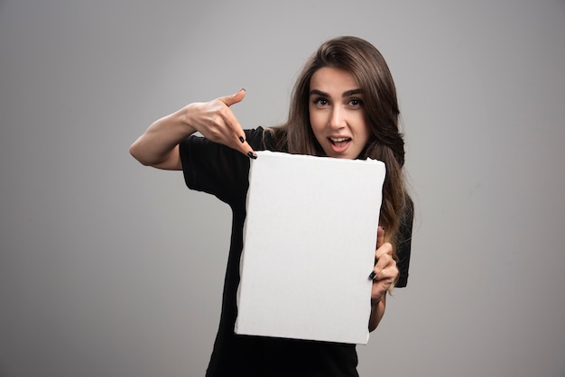 Free photo young woman pointing at empty canvas.