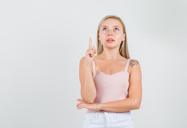 Young woman pointing finger up in singlet, mini skirt and looking focused.