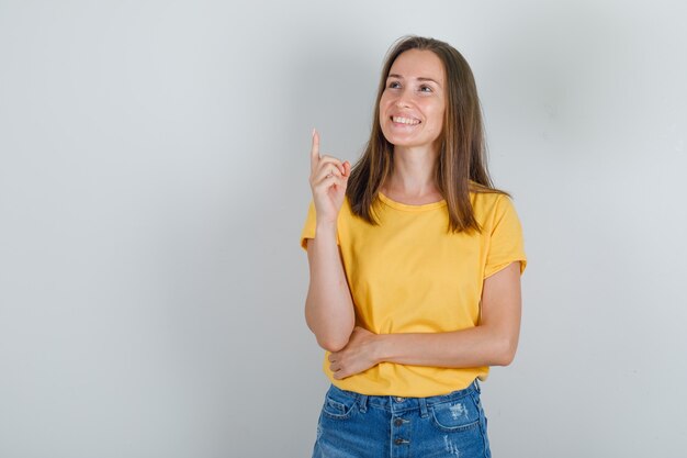 指を上に向けて、Tシャツで笑っている若い女性