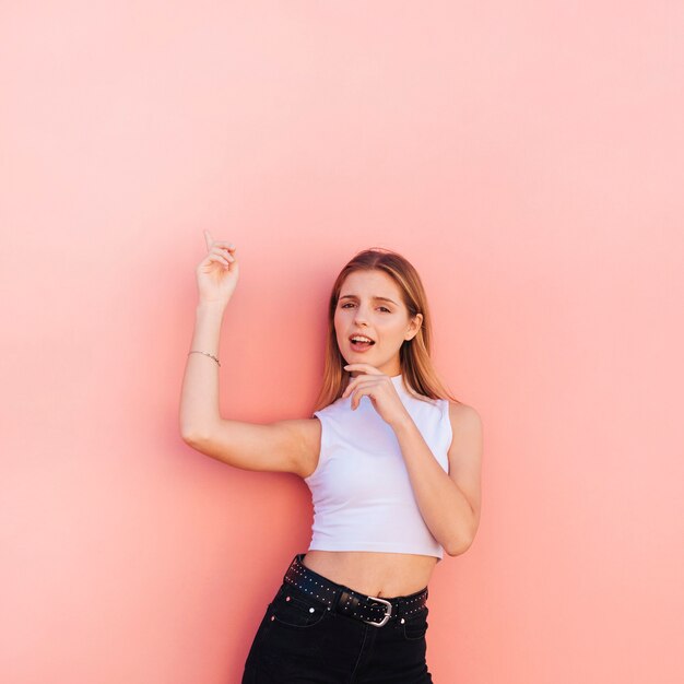 Young woman pointing fingers upward against colored backdrop