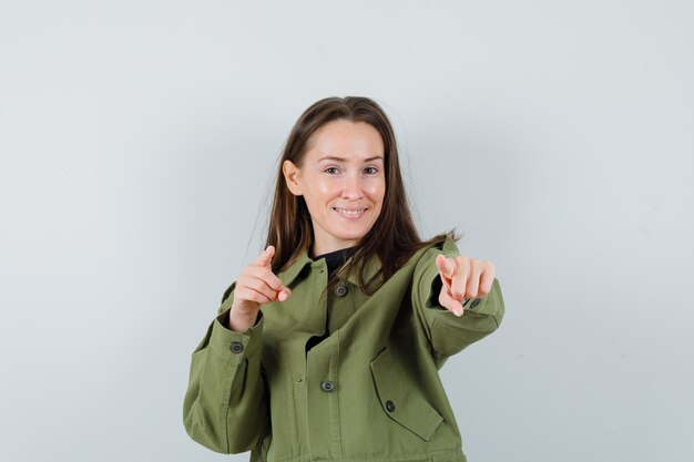 Молодая женщина, указывая на вперед в зеленой куртке и глядя довольна, вид спереди.