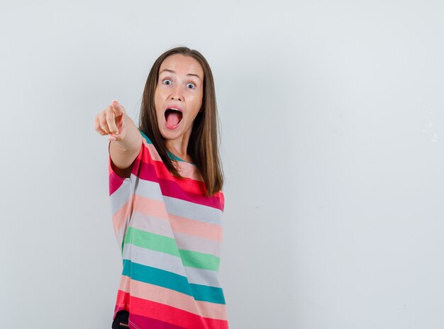 Young woman pointing at front in t-shirt and looking crazy. front view.