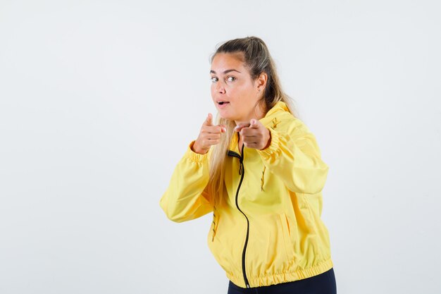 Young woman pointing at front in yellow raincoat and looking focused