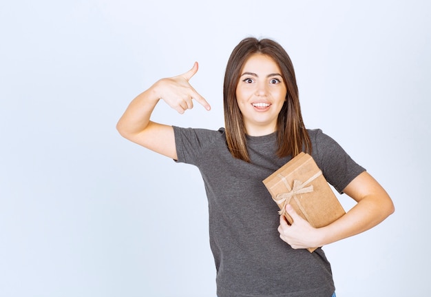 young woman pointing at a gift box with an index finger .