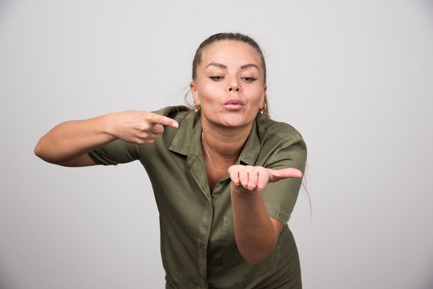 Young woman pointing at her hand on gray wall.