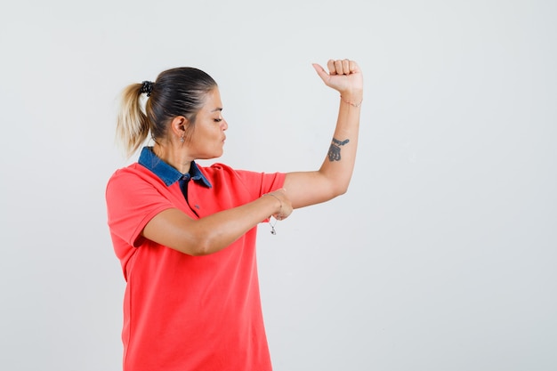 Young woman pointing her muscles in red t-shirt and looking serious , front view.