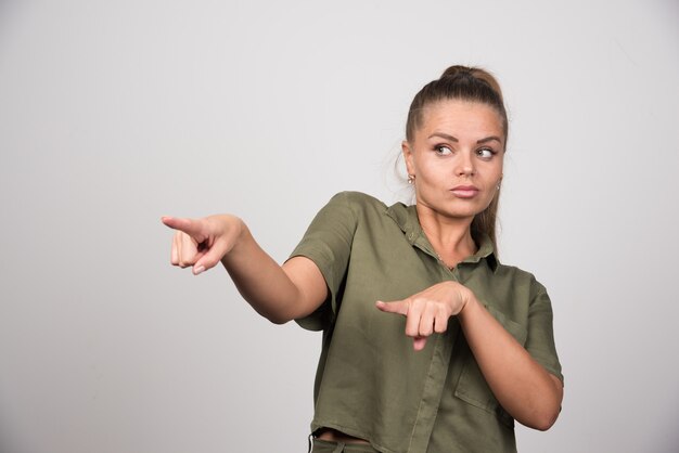 Young woman pointing at her side on gray wall.