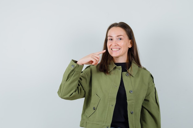 緑のジャケットの正面図で彼女の歯を指している若い女性。