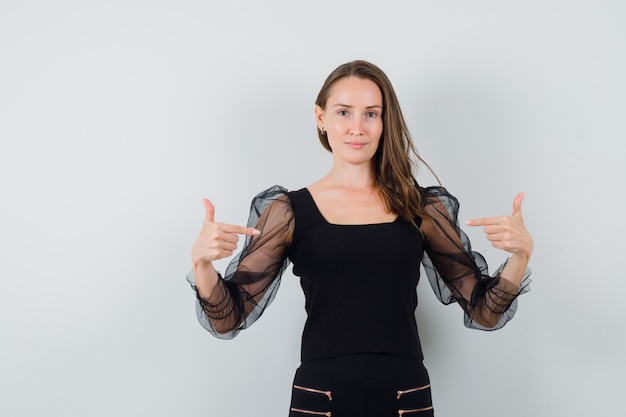 Young woman pointing at herself in black blouse and looking assured.