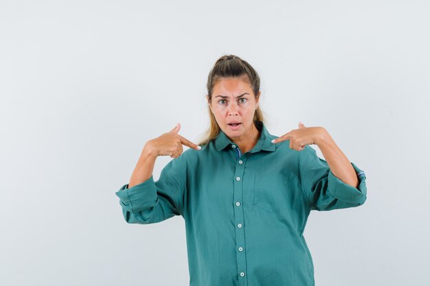 Young woman pointing at herself in blue shirt and looking aggressive