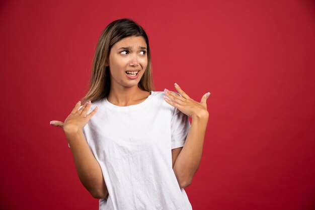 Young woman pointing at herself on red wall. 
