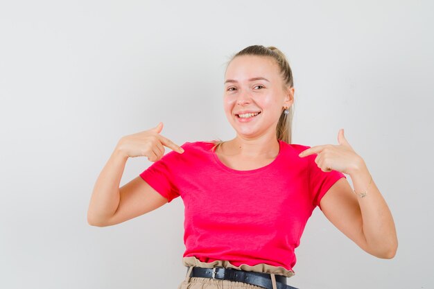 Young woman pointing at herself in t-shirts and pants and looking cheerful