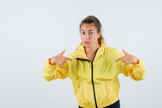 Young woman pointing at herself in yellow raincoat and looking attentive