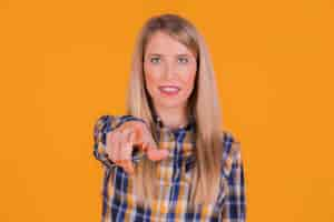 Free photo a young woman pointing his finger toward camera against an orange backdrop