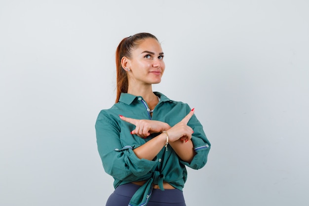 Free photo young woman pointing left and right, looking up in green shirt and looking hopeful. front view.