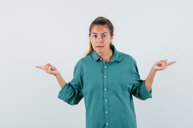 Young woman pointing opposite directions with index fingers in green blouse and looking cute