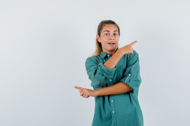 Young woman pointing at reverse sides in blue shirt and looking puzzled