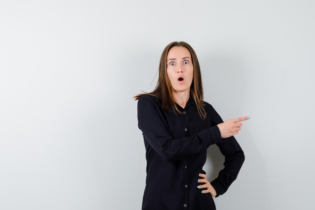 Young woman pointing right and looking scared