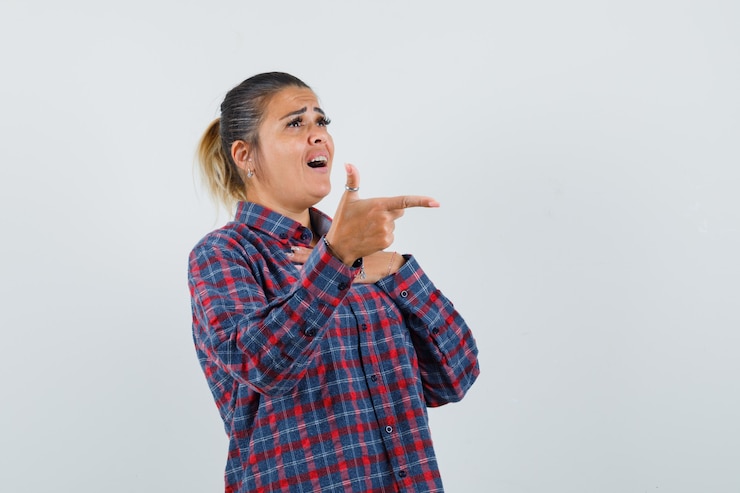 मुफ़्त फोटो young woman pointing right with index finger in checked shirt and looking pretty , front view.