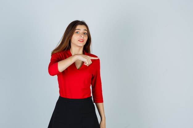 Young woman pointing right with index finger in red blouse