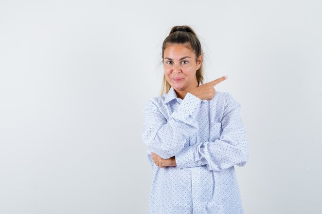 Young woman pointing right with index finger in white shirt and looking happy