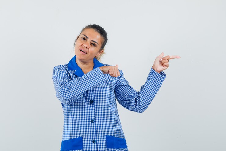 मुफ़्त फोटो young woman pointing right with index fingers in blue gingham pajama shirt and looking pretty , front view.
