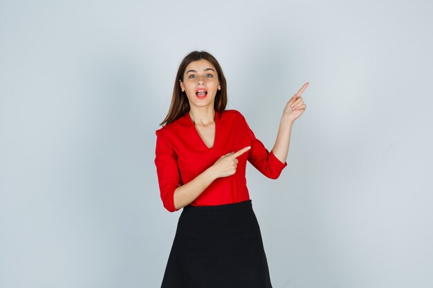 Young woman pointing right with index fingers in red blouse