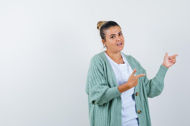 白いシャツとミントグリーンのカーディガンで人差し指で右を指して幸せそうに見える若い女性