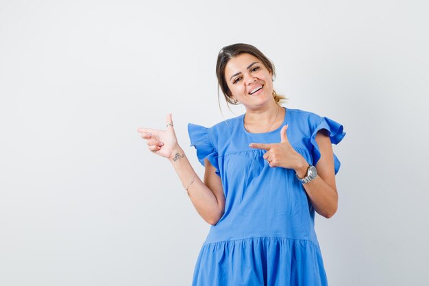 Young woman pointing to the side in blue dress and looking cheerful