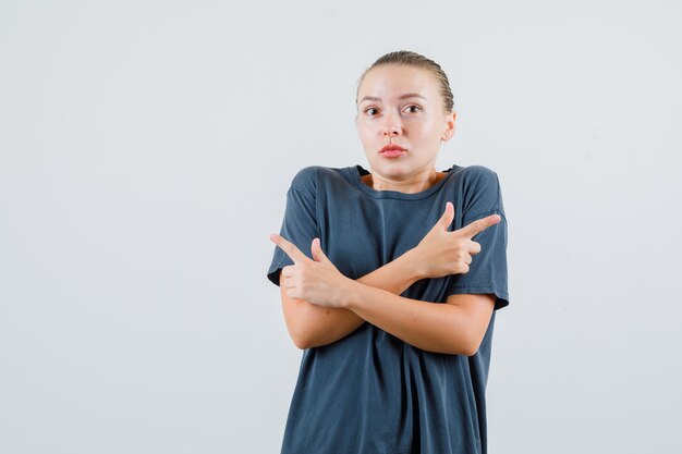 Young woman pointing to side in grey t-shirt and looking puzzled