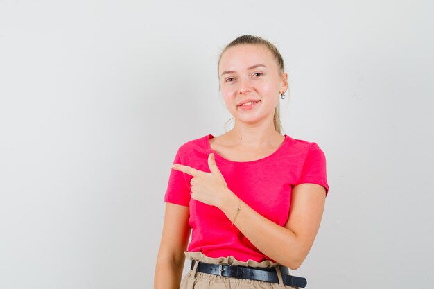 Young woman pointing to the side in t-shirts and pants and looking cheerful