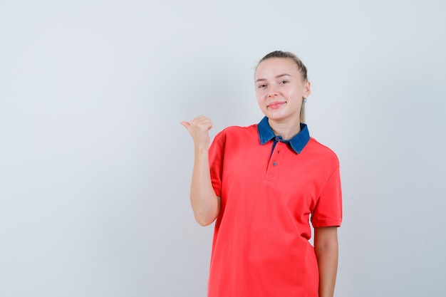 Молодая женщина указывая в сторону большим пальцем в футболке и выглядит весело