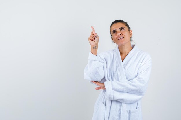 Young woman pointing up in bathrobe and looking confident